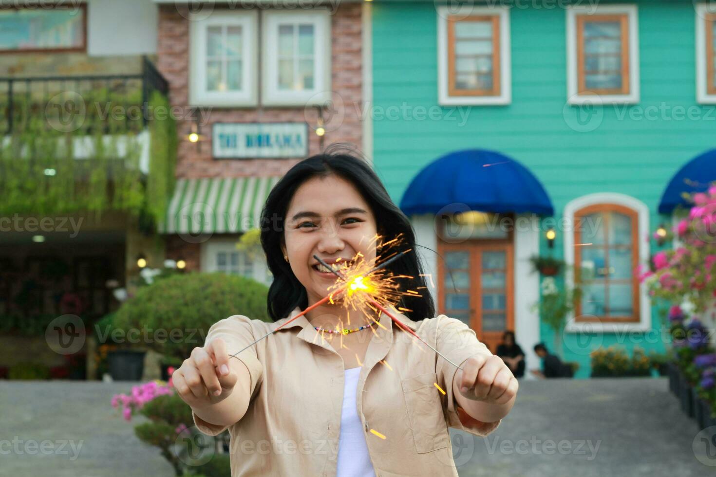 Lycklig ung asiatisk kvinna innehav sparkler fira ny år eve i årgång hus gård, utomhus- trädgård foto