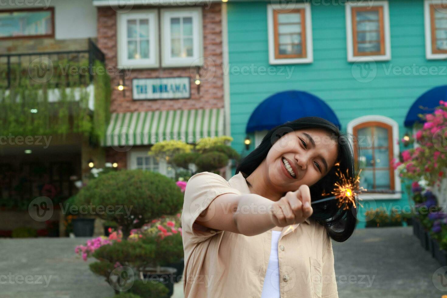 Lycklig ung asiatisk kvinna innehav sparkler njut av ny år eve firande i utomhus- trädgård av färgrik årgång hus i kväll foto