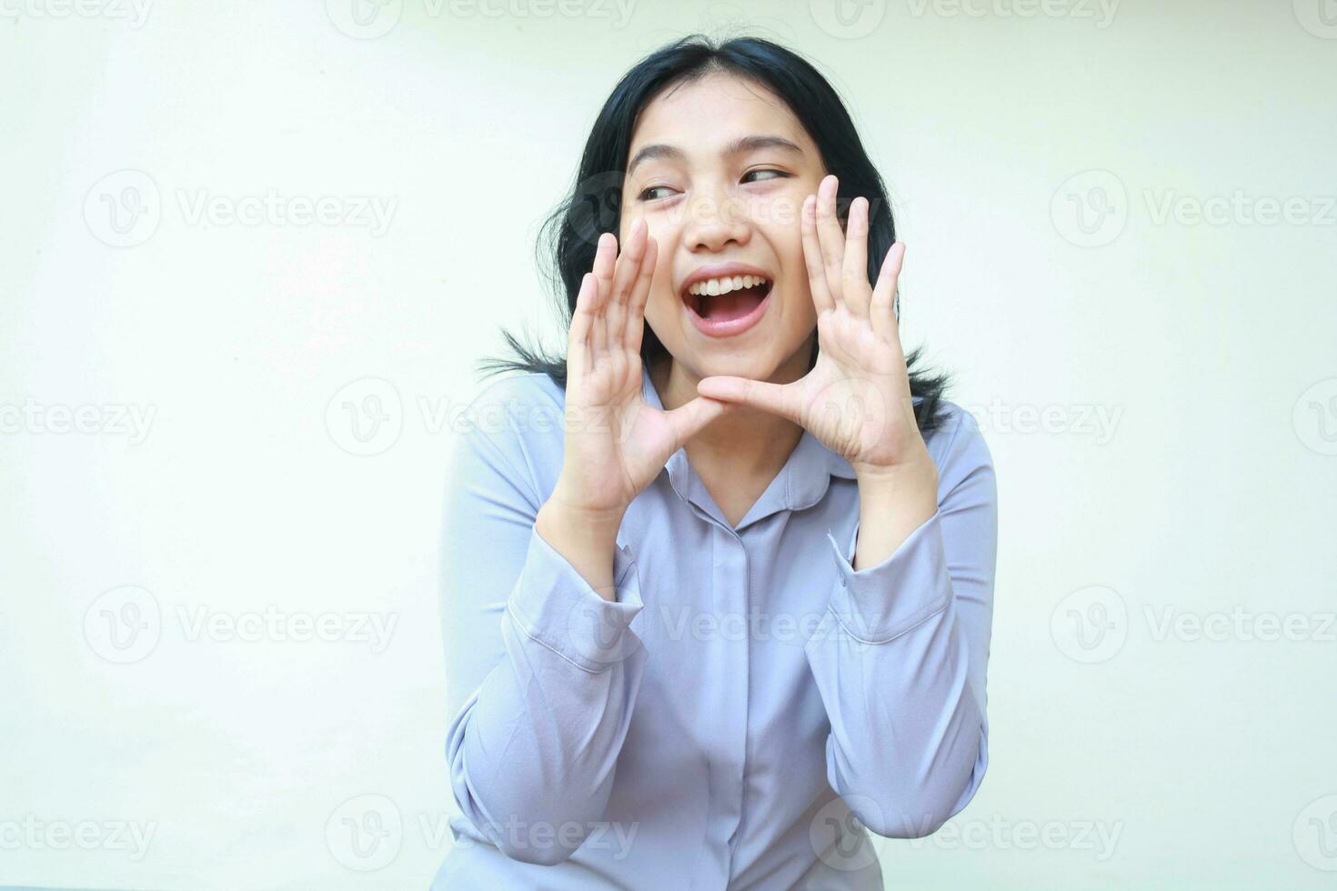 bild av Söt asiatisk ung företag kvinna skrikande till kamera med öppen mun ser bort, främja produkt, ha på sig formell lila skjorta stående över isolerat vit bakgrund foto
