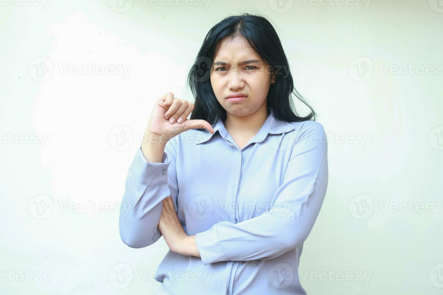 förvirrad asiatisk ung företag kvinna ger tummen ner ser åt sidan med vikta ärm visa upprörd uttryck fällning missnöjd bär formell skjorta stående över isolerat vit bakgrund foto