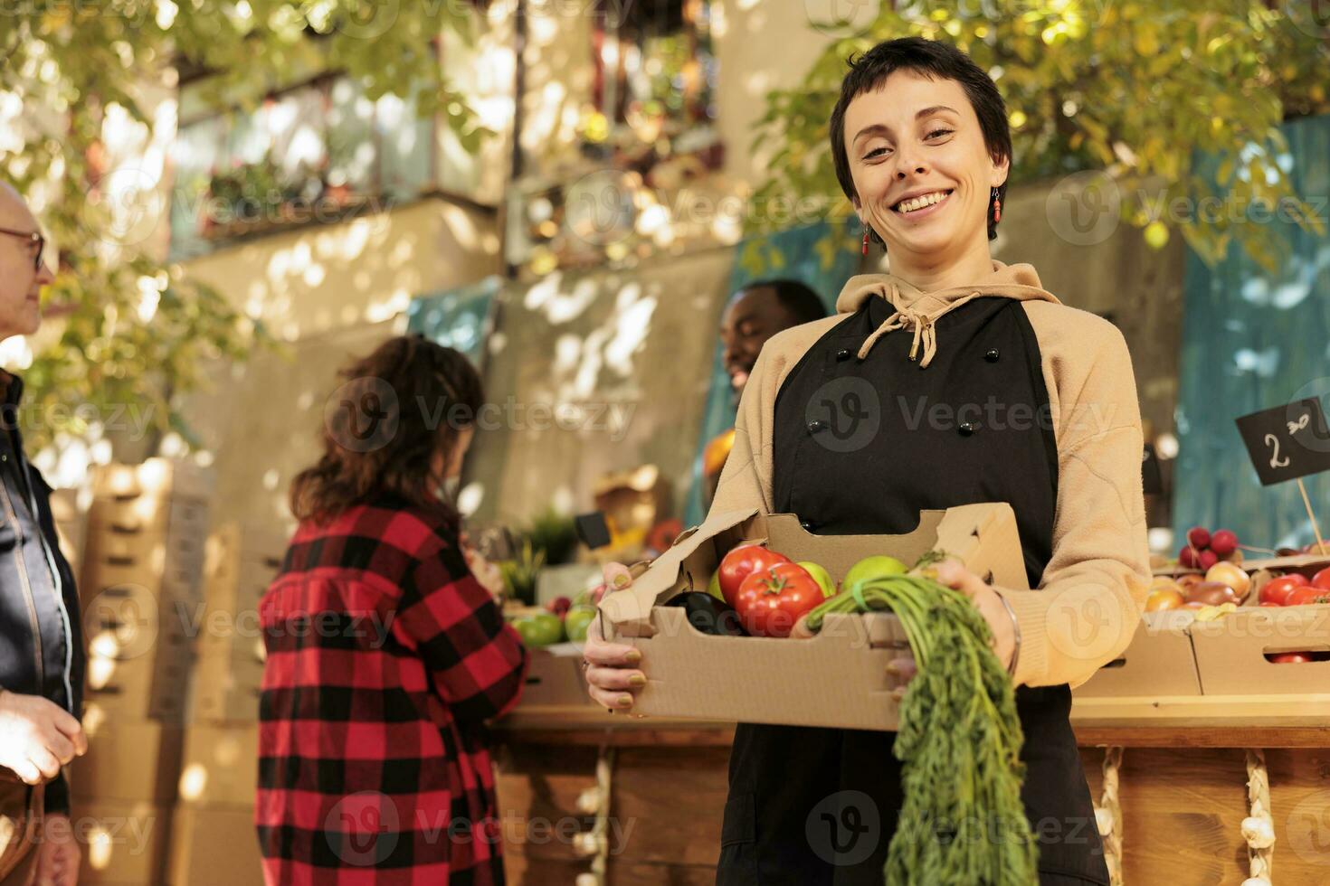 ung glad säljare frukt och grönsaker marknadsföra stå ägare som visar färsk organisk producera låda och leende på kamera. kvinna jordbrukare försäljning friska lokal- mat från vid vägkanten stå, bio Produkter. foto