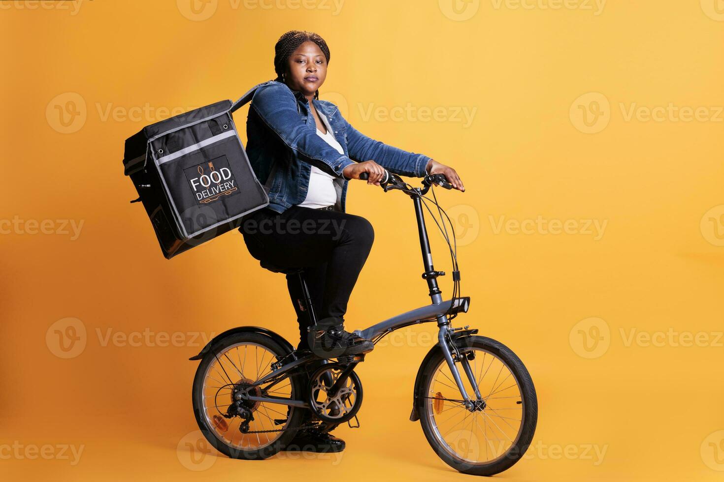 mat leverans anställd ridning cykel medan bärande hämtmat termisk ryggsäck redo till leverera beställa till klient under lunch tid, stående över gul bakgrund. mat service och transport foto