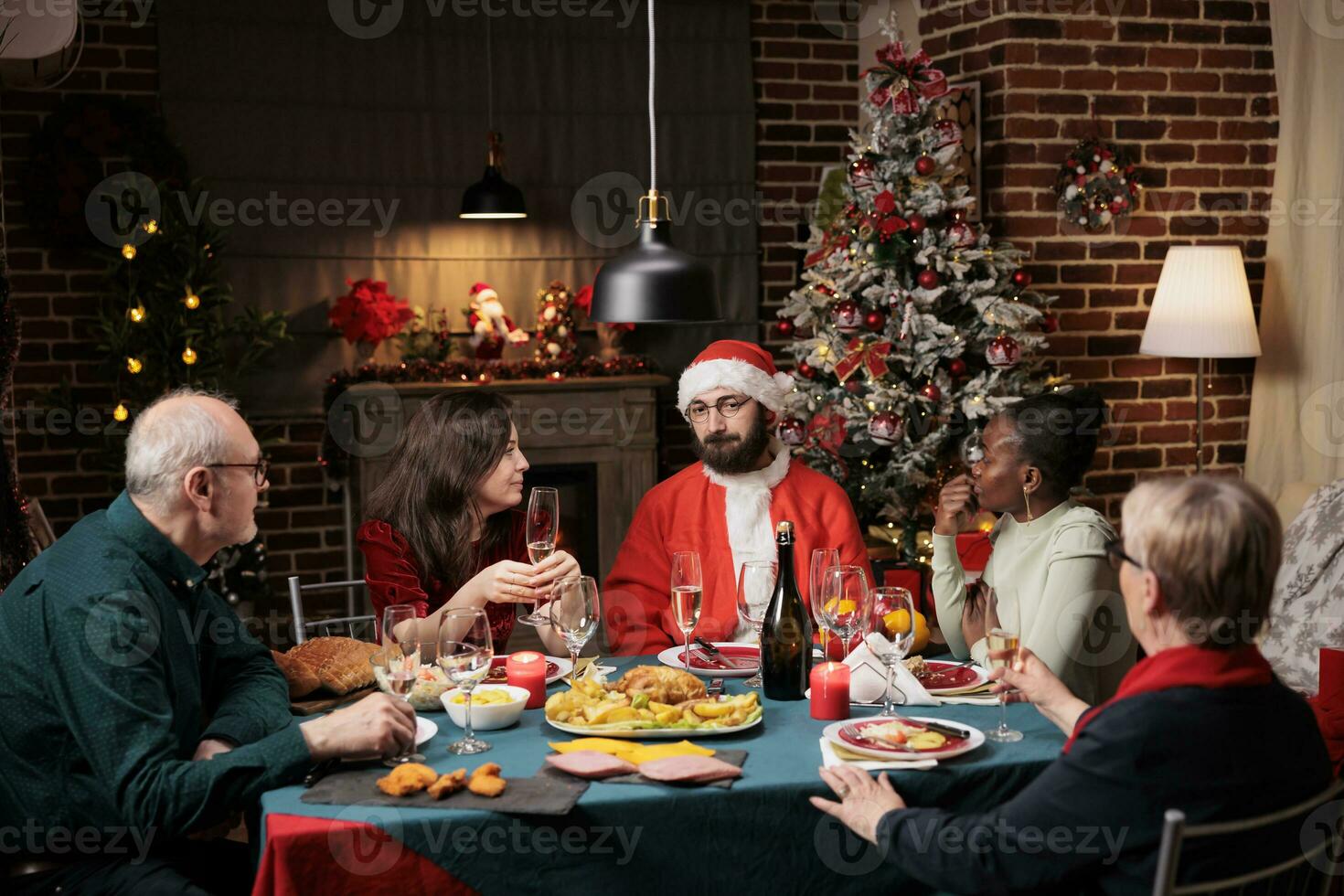 person santa claus cosplay på middag framställning människor skratt och fira jul eve fest tillsammans. senior människor, vänner och familj sammankomst runt om tabell till äta och dryck på Semester. foto
