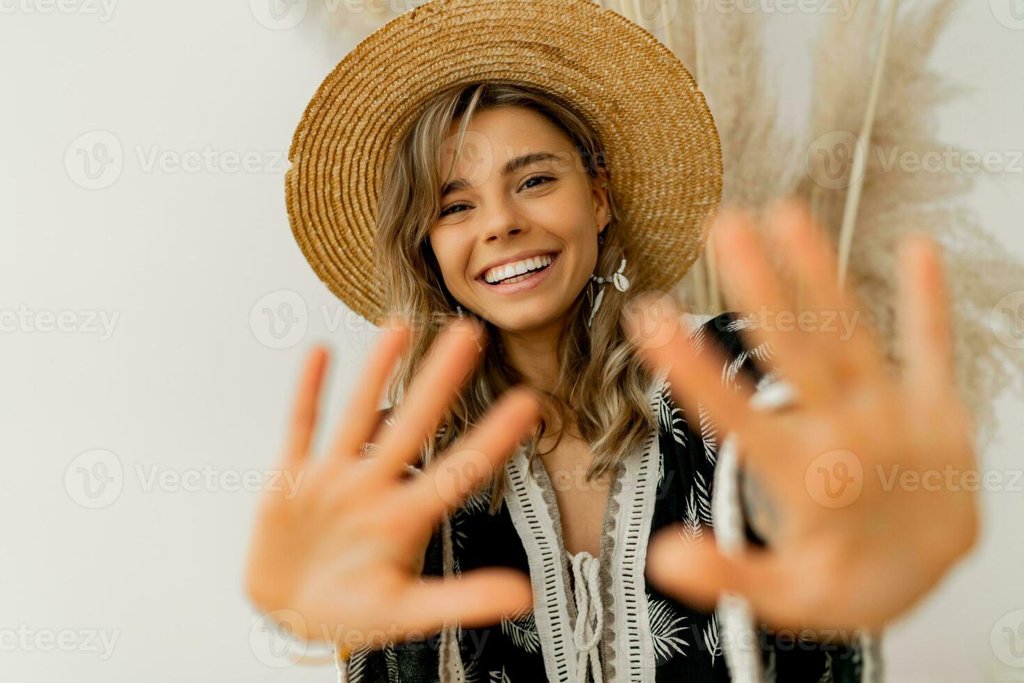 lekfull glad kvinna i sugrör hatt dra händer till de kamera. vit bakgrund. boho utrusta. eleganta sommar tillbehör. foto
