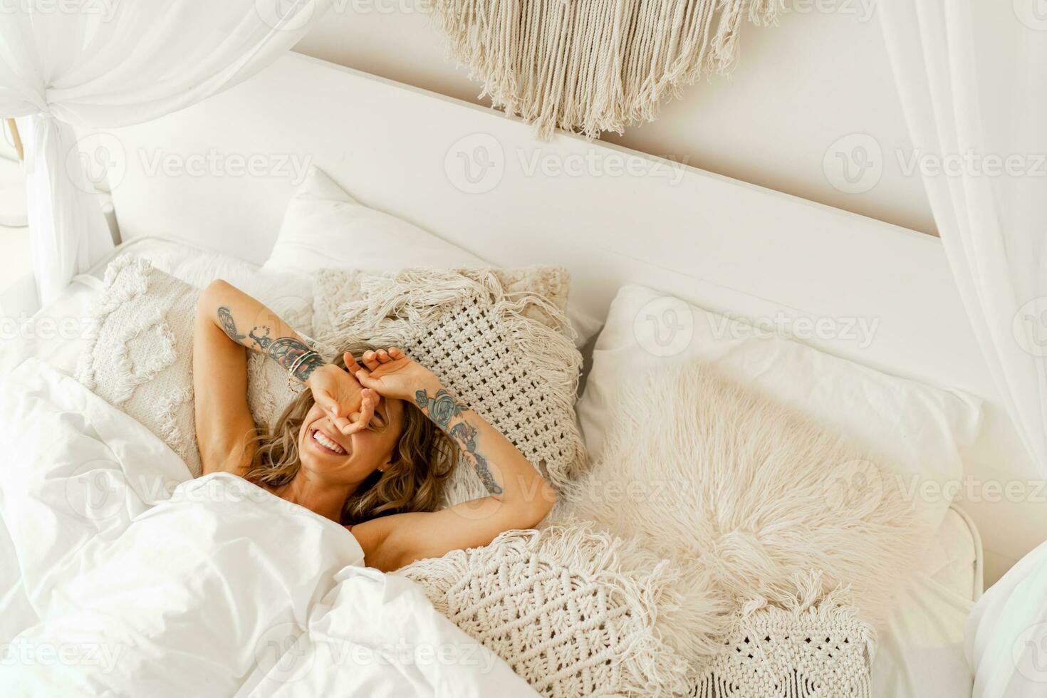skrattande kvinna kylning i henne säng. tatoo på händer. mysigt Hem livsstil. foto