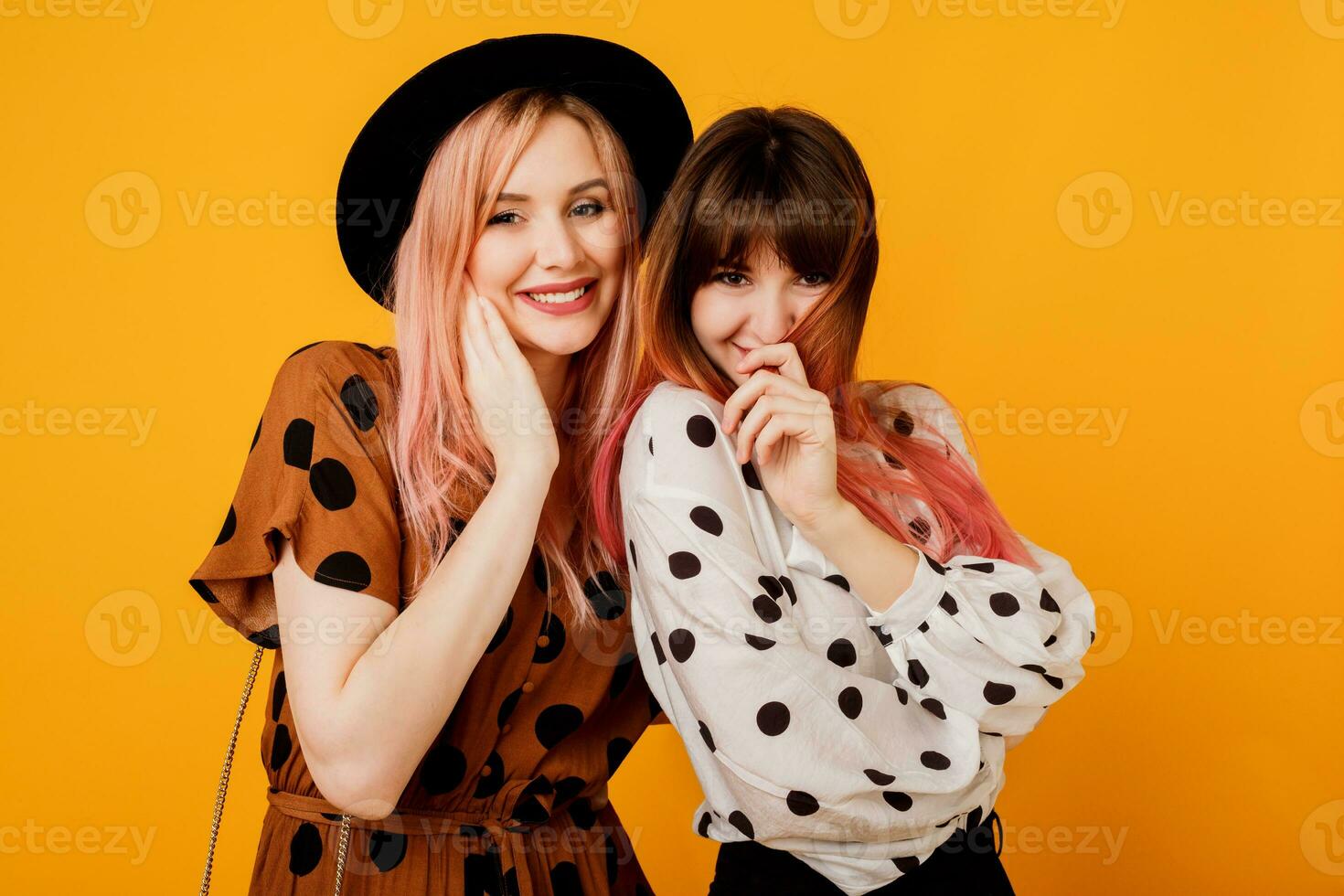 modern studio skott av två eleganta kvinnor med rosa hårstrån Framställ över gul bakgrund. extatisk känslor. handla och vänskap begrepp. foto