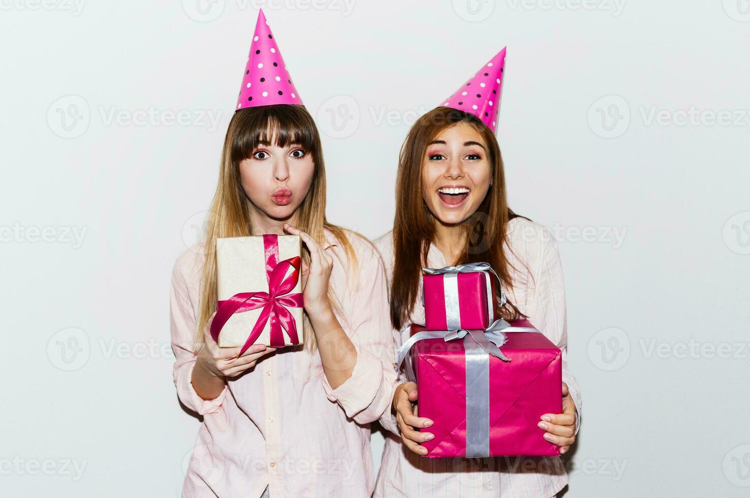 pyjamas födelsedag fest. vänner har roligt och innehav gåva lådor. överraskning ansikte, exits känslor. flickor bär stötta fest hattar. inomhus. foto