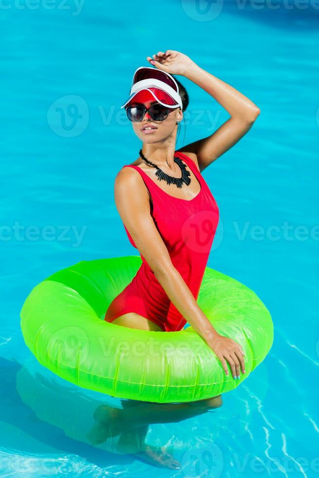sexig solbränd kvinna i röd baddräkt har roligt och njuter sommar i Fantastisk stor simning slå samman. eleganta transparent keps. strand fest. foto