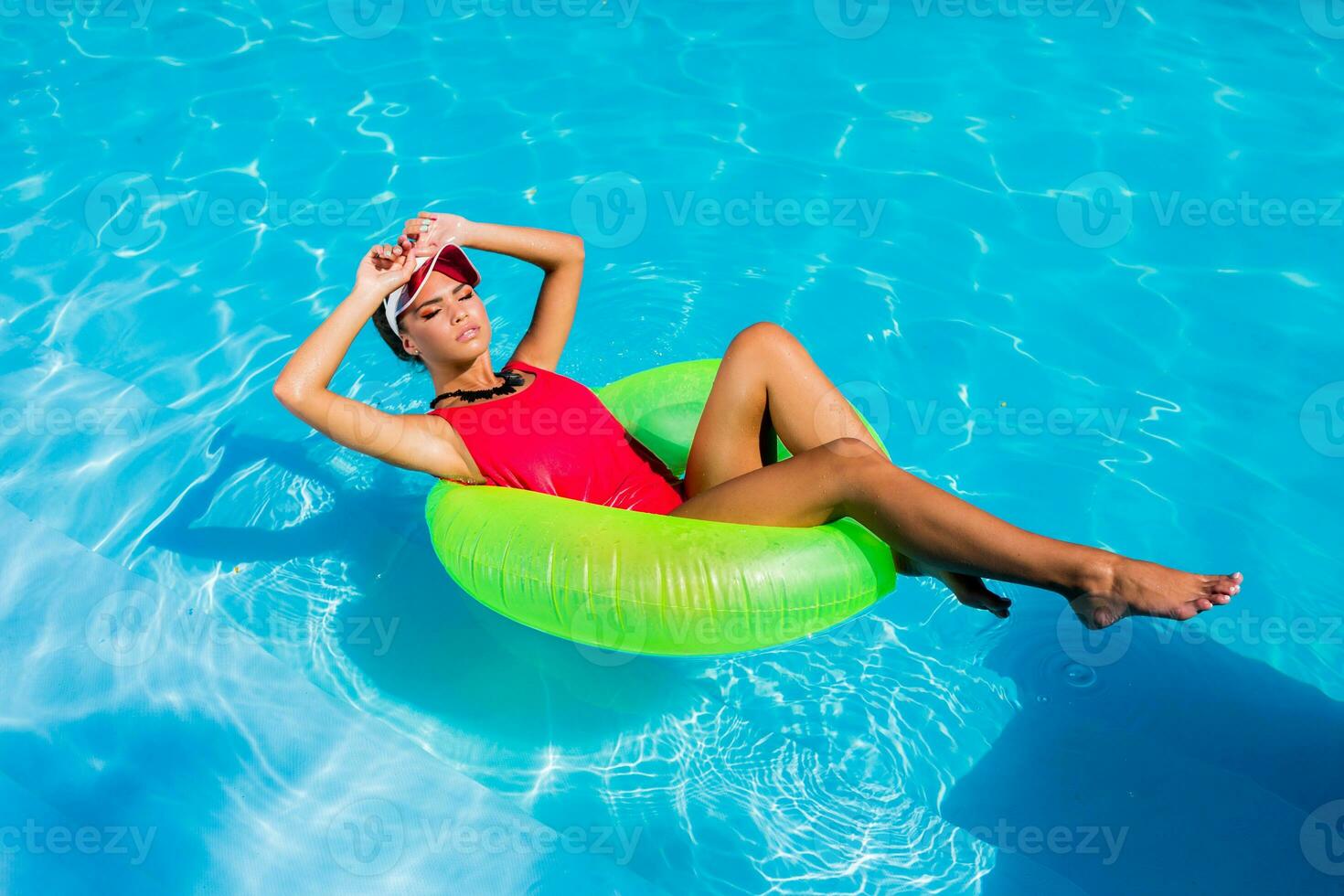 sexig solbränd kvinna i röd baddräkt har roligt och njuter sommar i Fantastisk stor simning slå samman. ung Söt flicka simning på uppblåsbar ringa. eleganta transparent keps. strand fest. foto