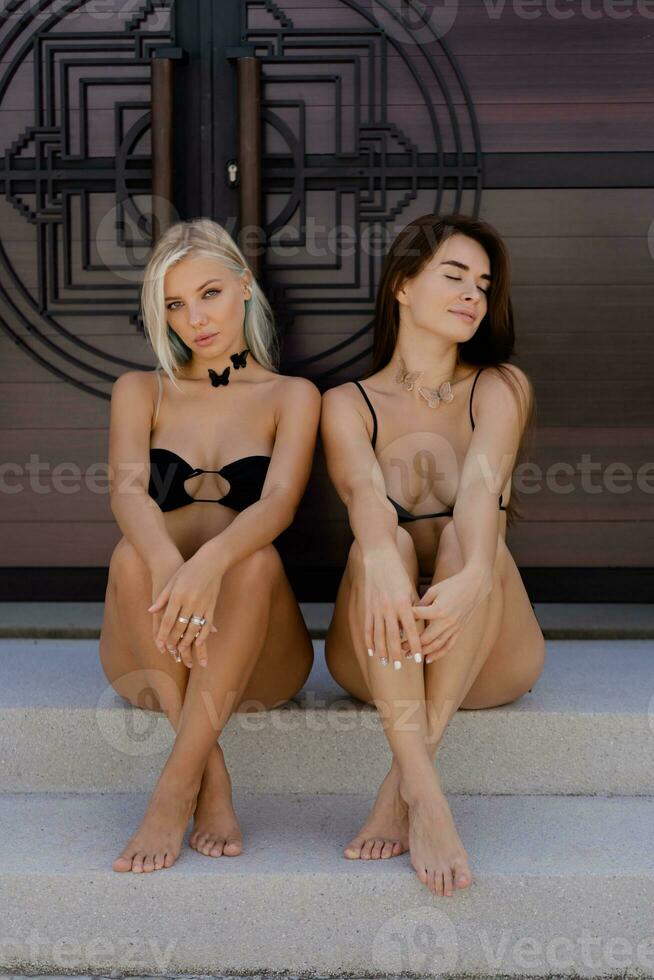 två sexig modeller Framställ utomhus- i elegant svart badkläder. blond och brunett kvinnor enjiong sommar semestrar. foto