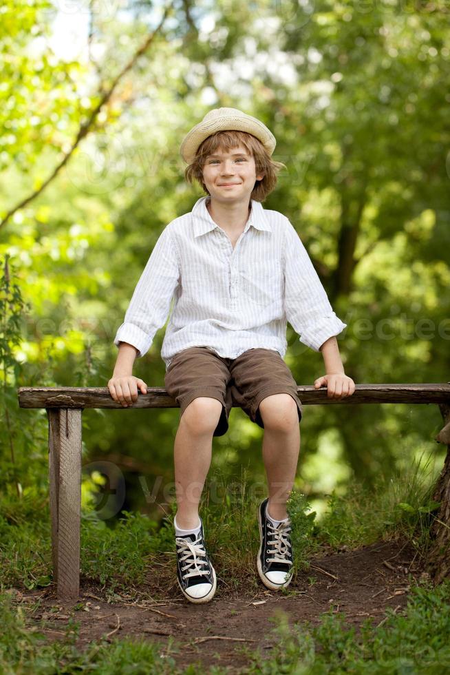 pojke i hatten och shorts sitter på en bänk foto