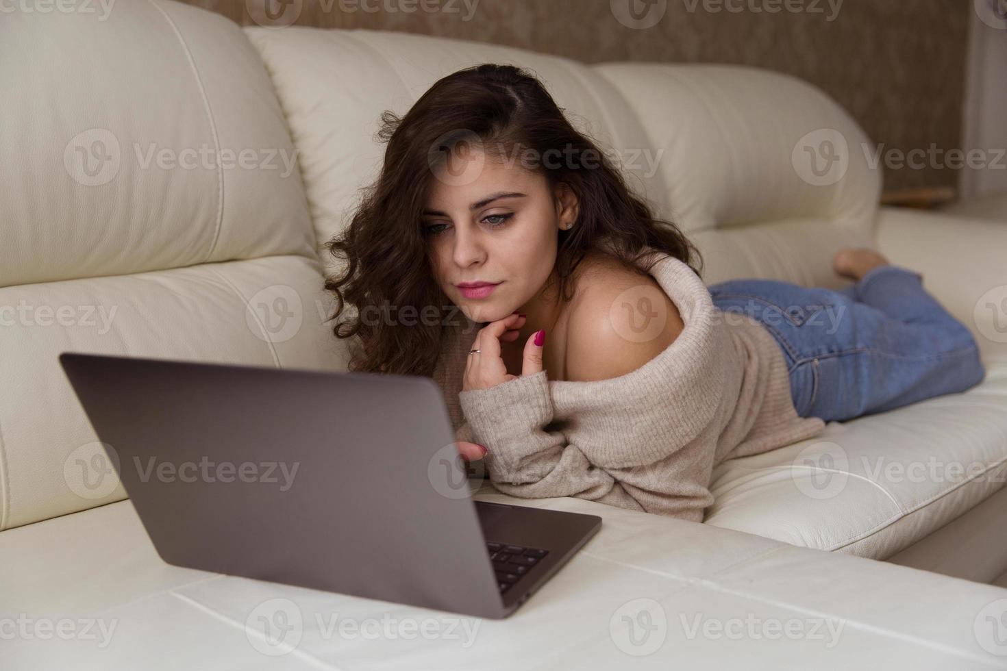 kvinna ligger på soffan med bärbar dator foto