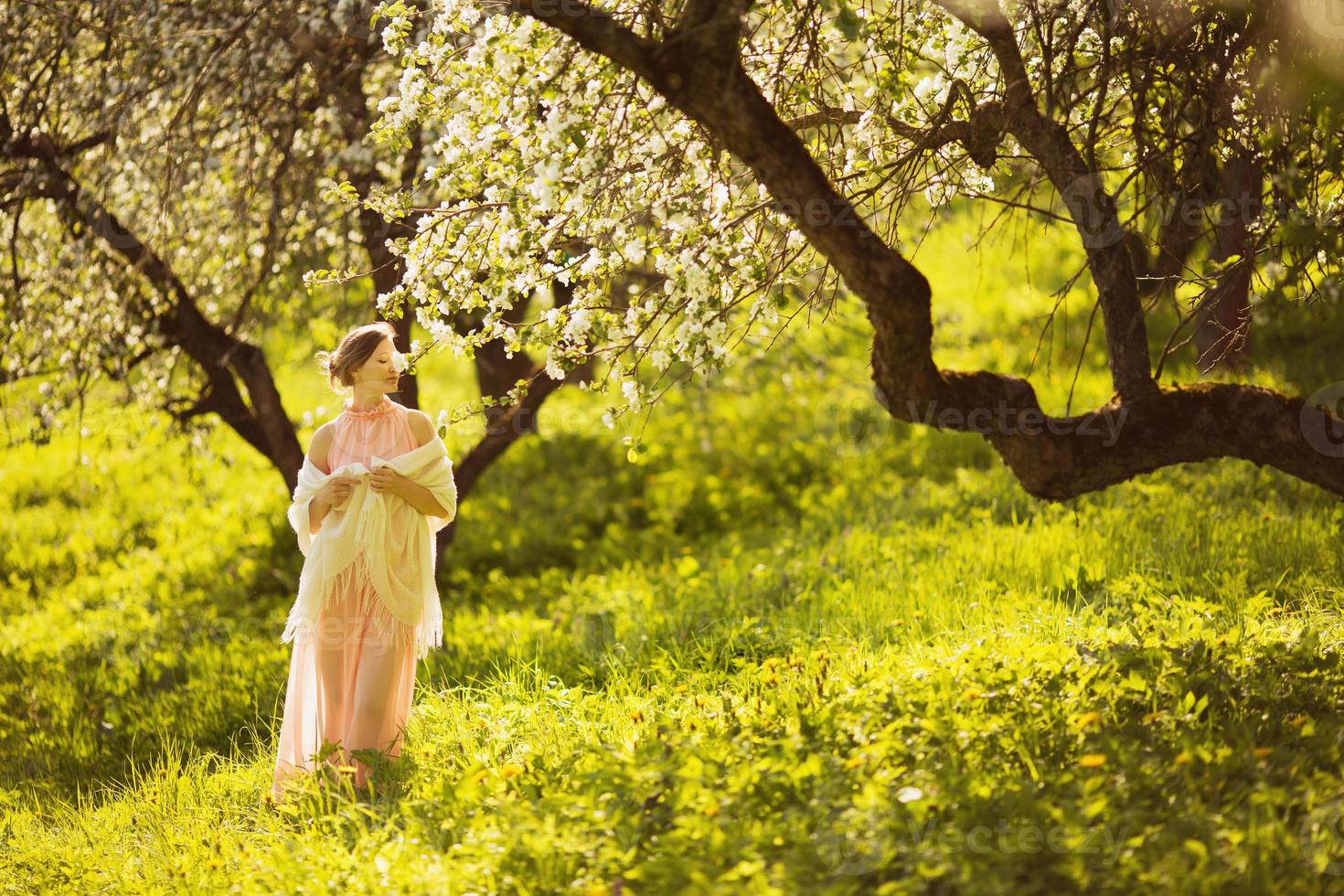glad ung kvinna som luktar en blomma på ett äppelträd foto