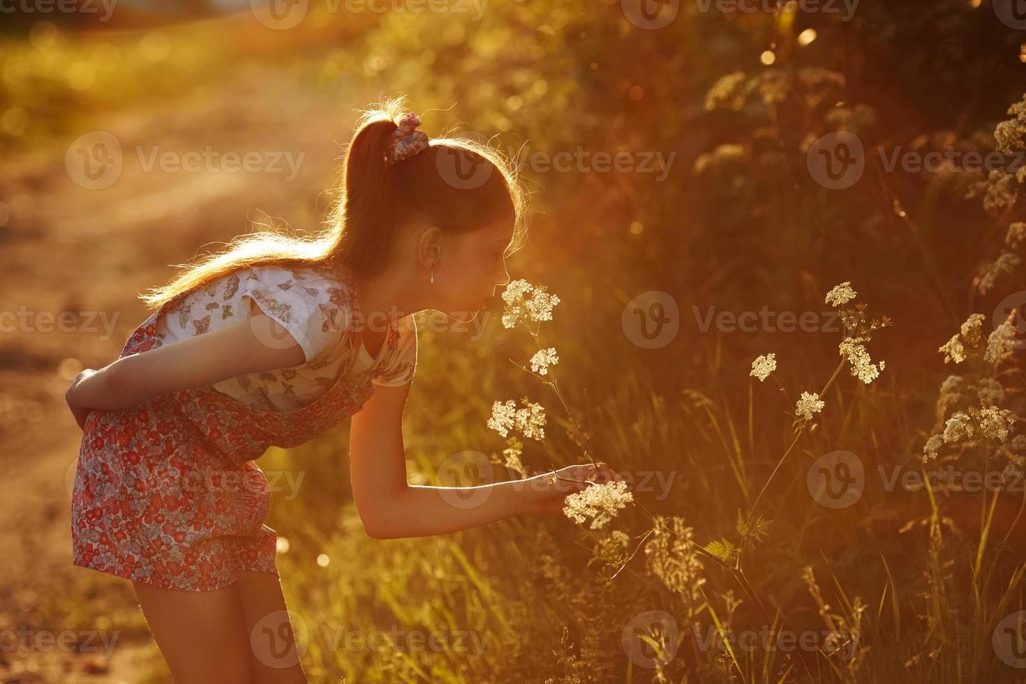 liten flicka som luktar en vild blomma foto