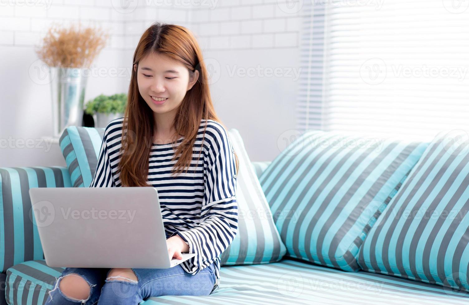 ung asiatisk kvinna som använder bärbar dator på fritiden på soffan i vardagsrummet. foto