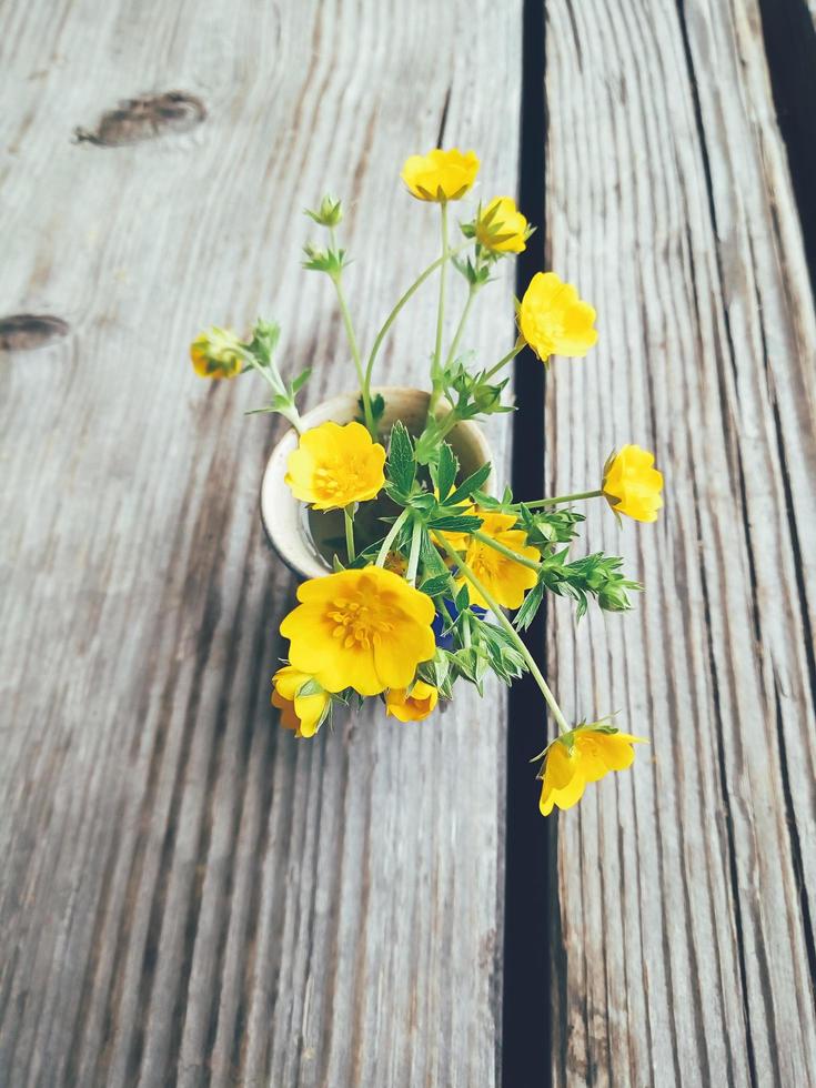 gula viola blommor i blå keramik kopp, på trä veranda bakgrund. stilleben i rustik stil. närbild. sommar eller vår i trädgården, landsbygdens livsstilskoncept. vertikal bild foto