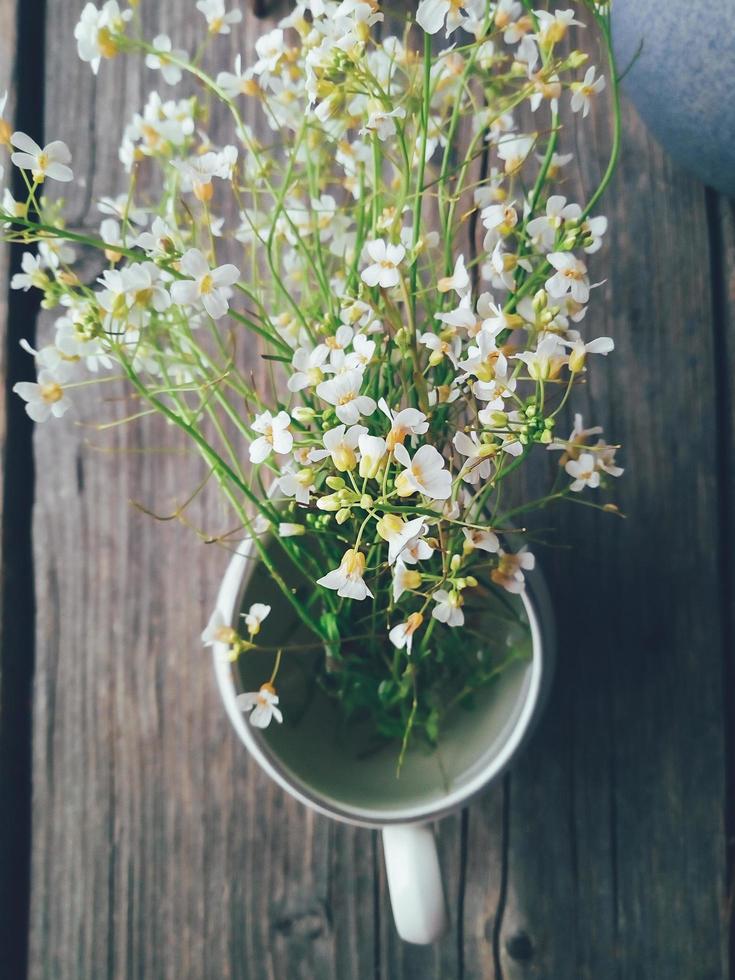 vilda färska blommor i porslinskanna, på blå träbakgrund. dagsljus. stilleben i rustik stil. landsbygdens livsstil, semester, semester koncept. selektivt fokus ovanifrån foto