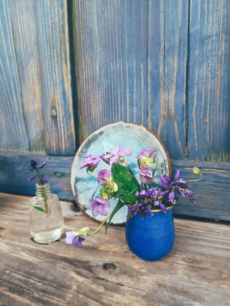 lila vilda blommor i blå keramisk vas, på träverandabakgrund. stilleben i rustik stil. närbild. sommar eller vår i trädgården, landsbygdens livsstilskoncept. kopiera utrymme foto