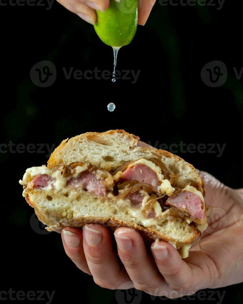 smörgås med bacon, lök och ost i hand på en svart bakgrund foto