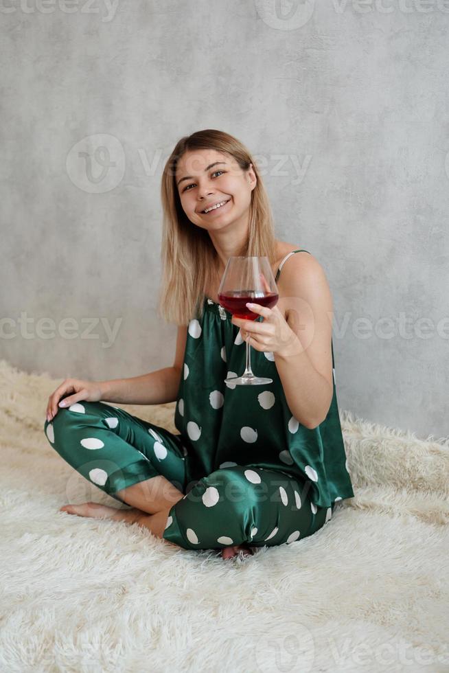 flicka i grön pyjamas i sängen med ett glas rött vin foto