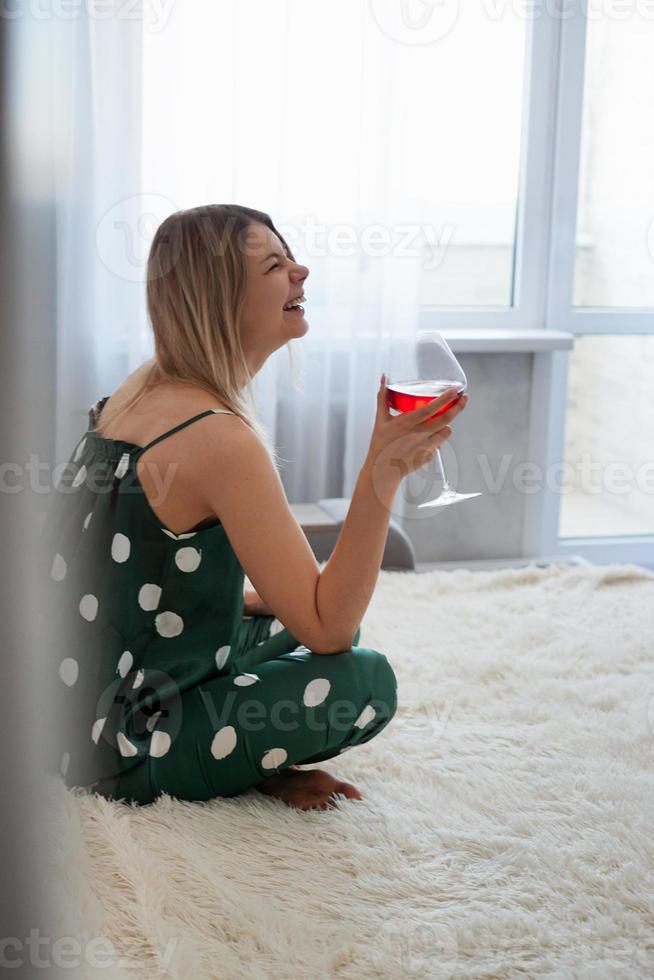 flicka i grön pyjamas i sängen med ett glas rött vin foto