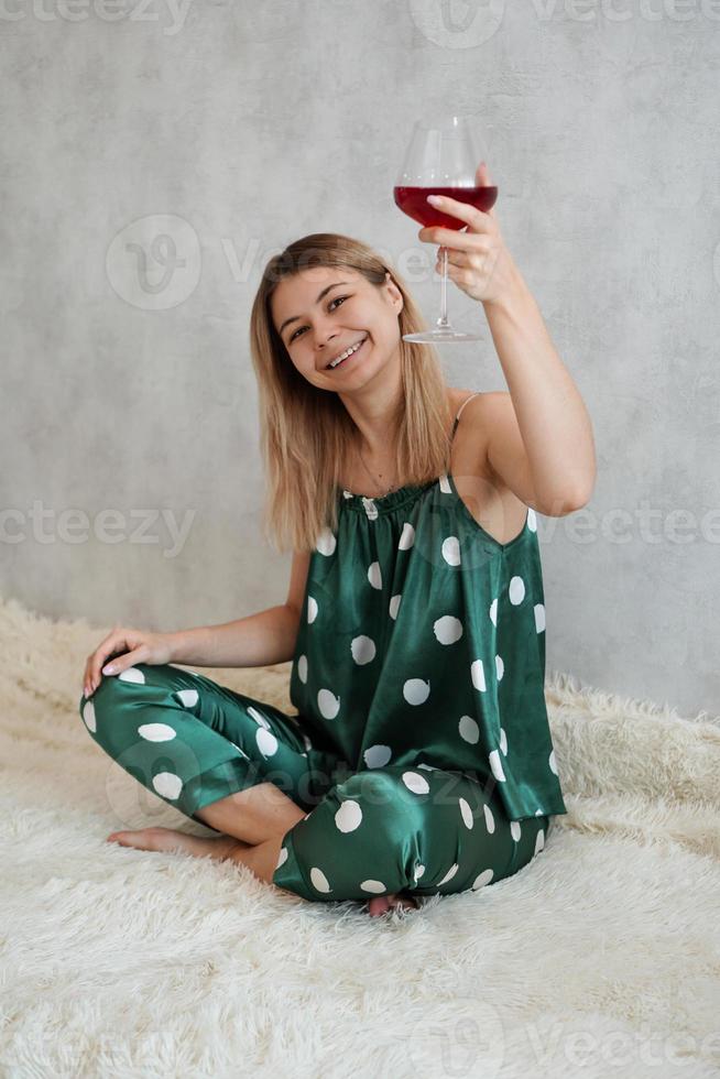 flicka i grön pyjamas i sängen med ett glas rött vin foto