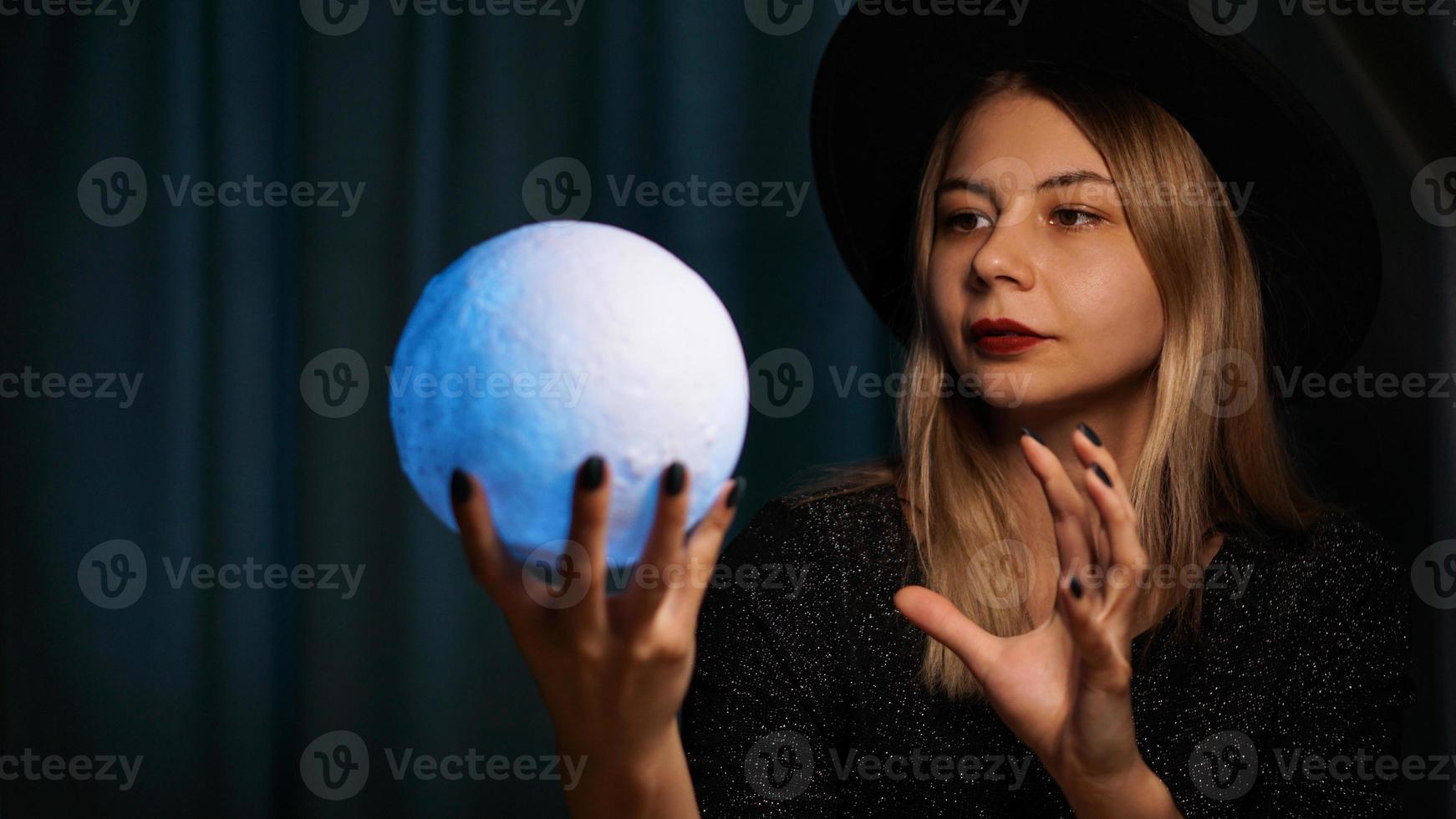 en ung kvinna spåkvinna i en hatt håller en magisk boll. foto