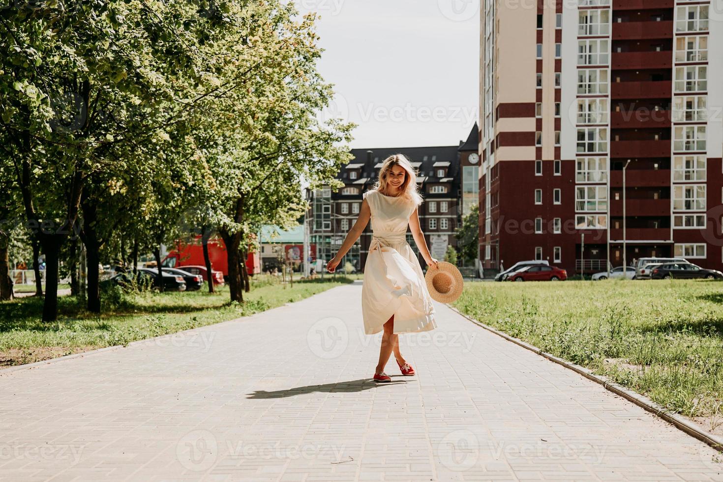 en vacker blondin går genom en stad. kvinna i vit klänning foto