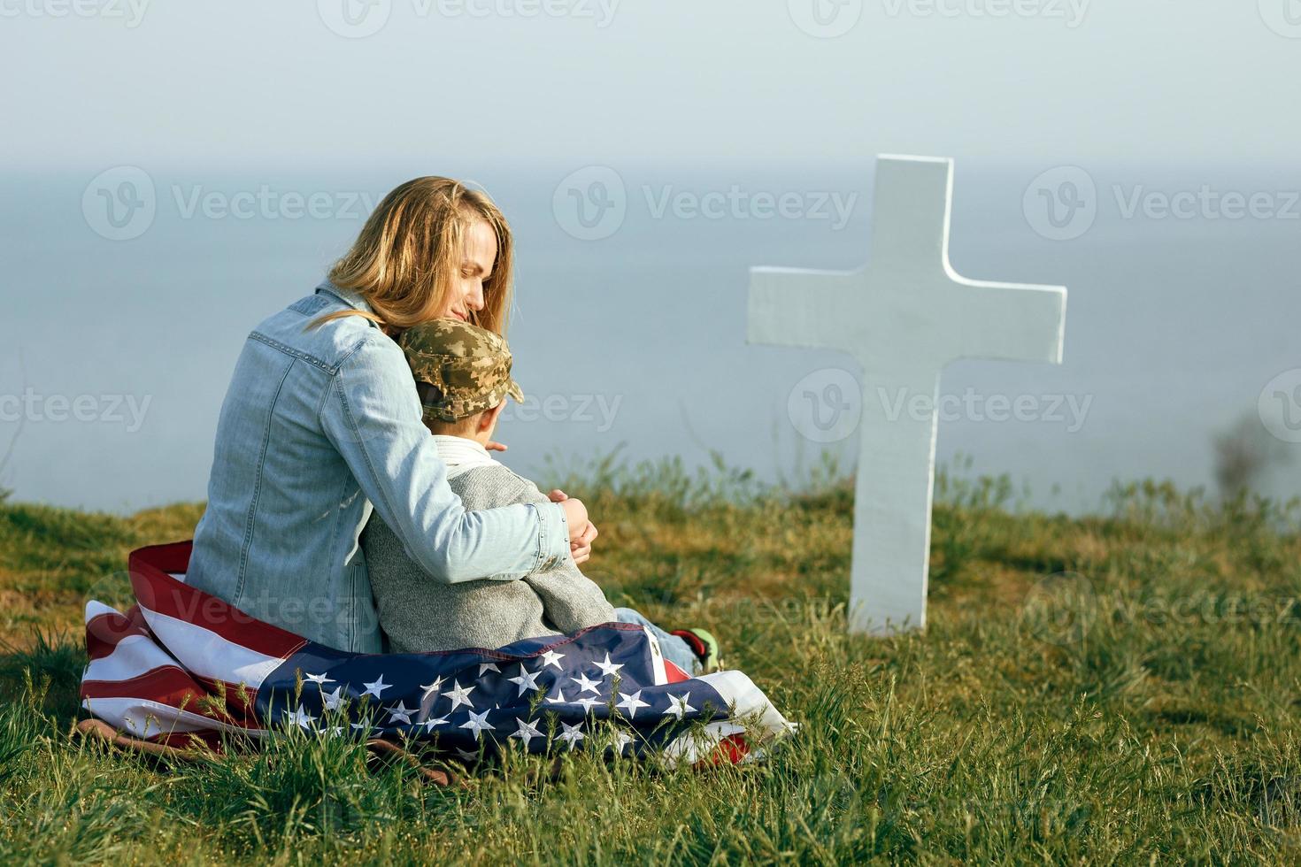 mamma och son sitter på en soldats grav foto