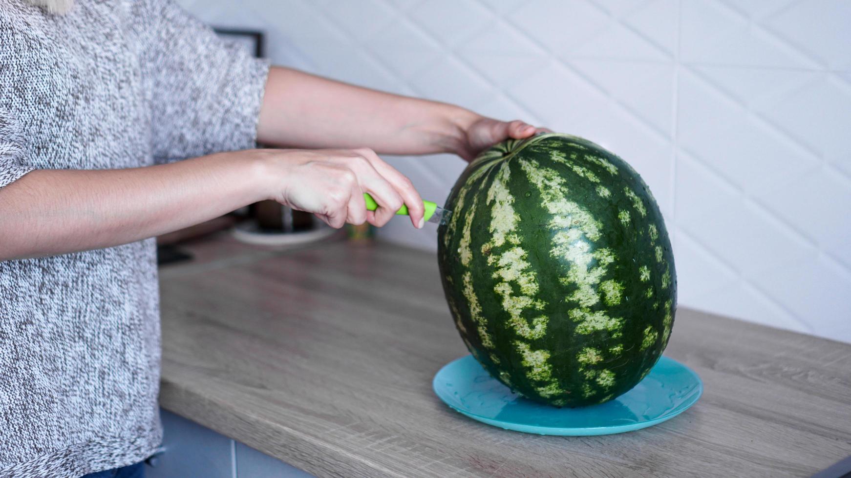 närbild av kvinna som skär vattenmelon i köket foto