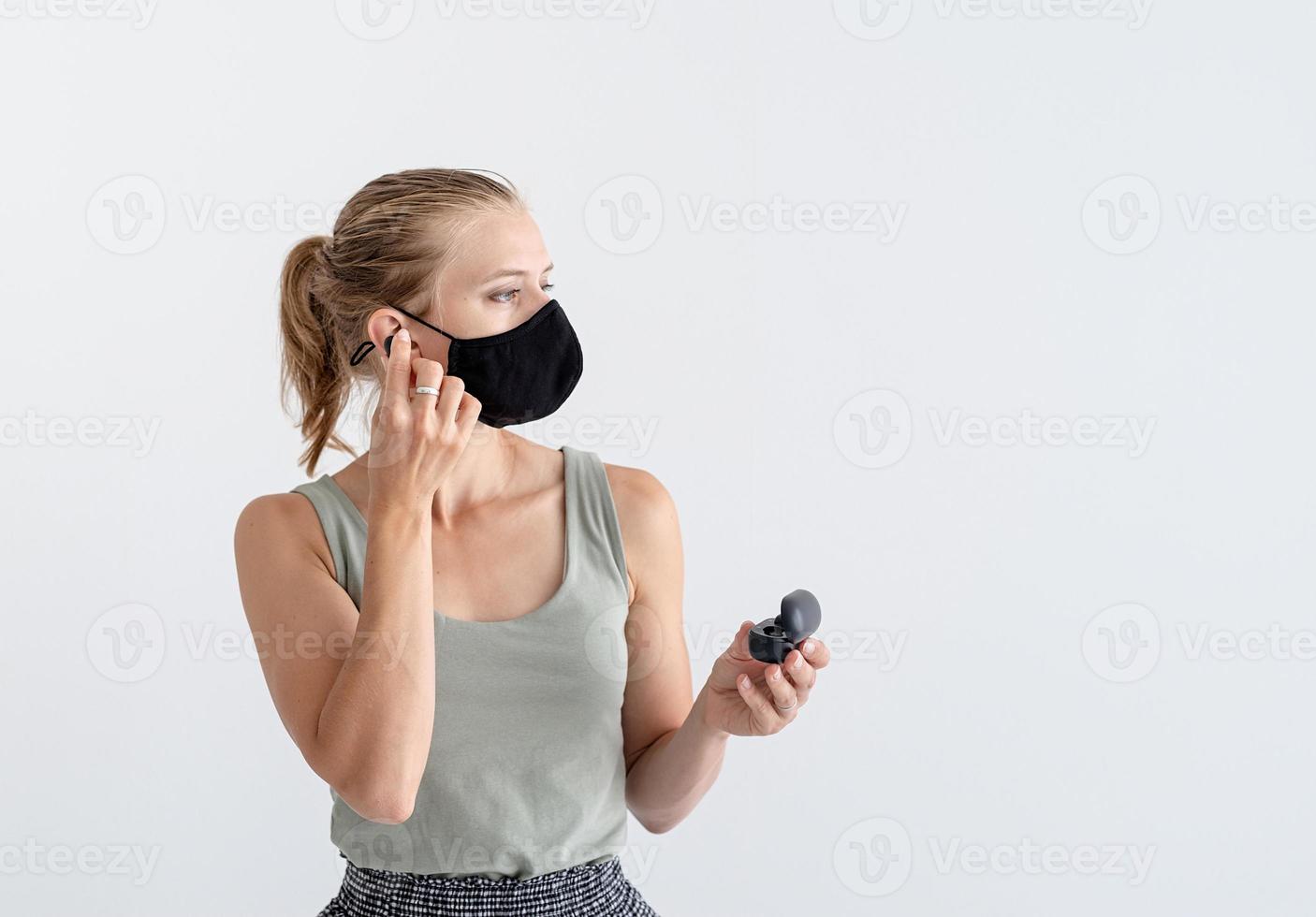 ung kvinna i en skyddande mask som håller trådlösa öronsnäckor foto