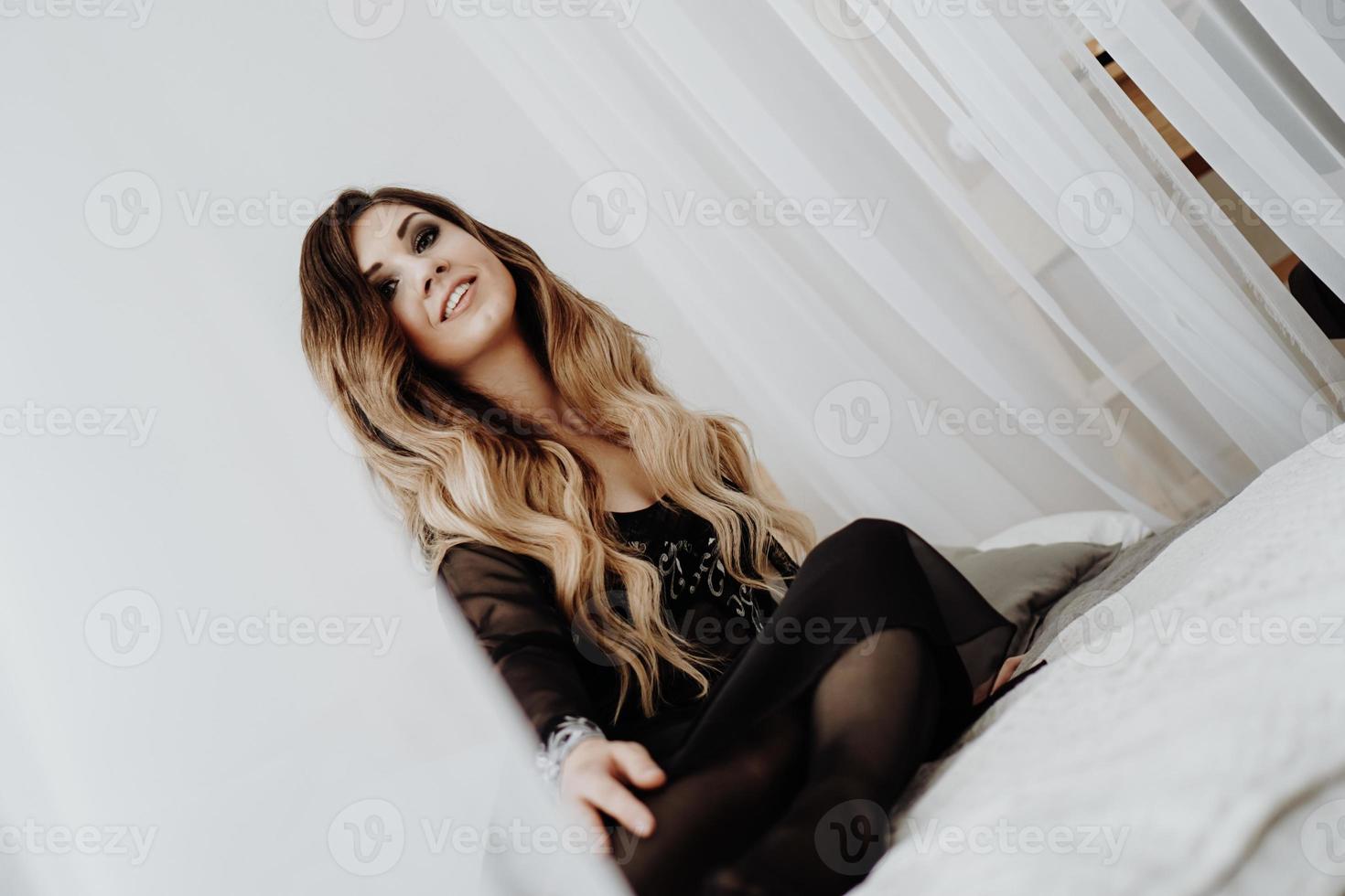 vacker sexig brun lockigt långt hår kvinna poserar i sängen foto