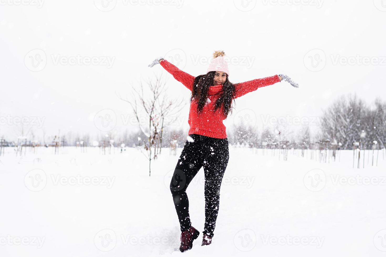 ung brunettkvinna i röd tröja som leker med snö i parken foto