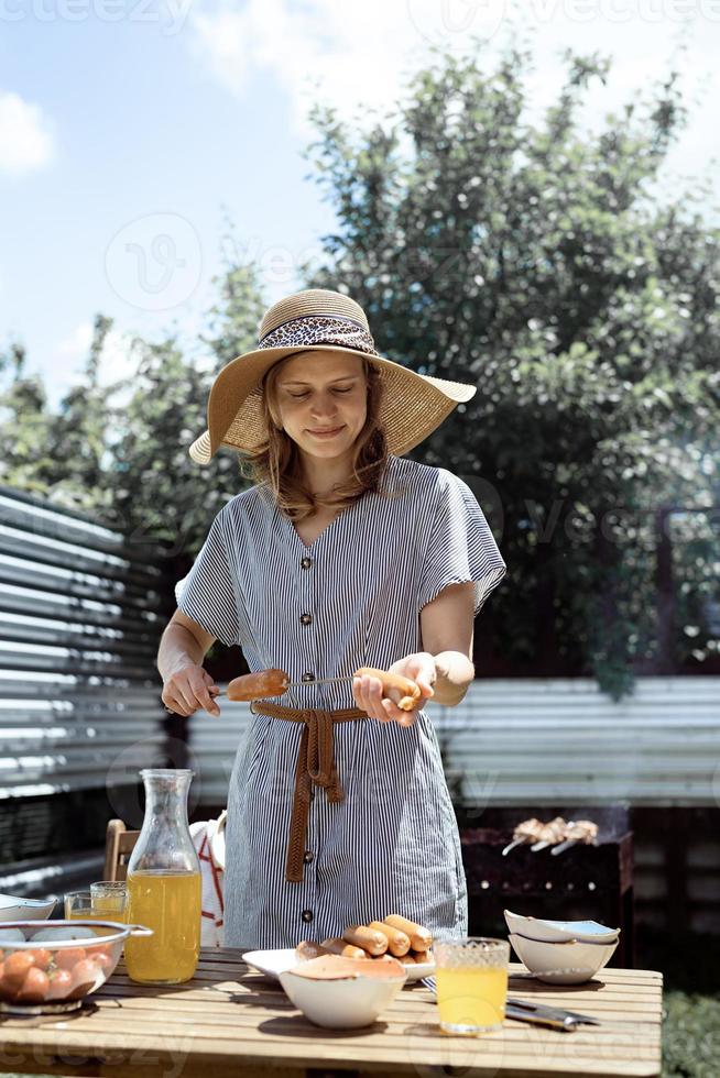 ung kvinna i sommarhatt som grillar kött utomhus på bakgården foto