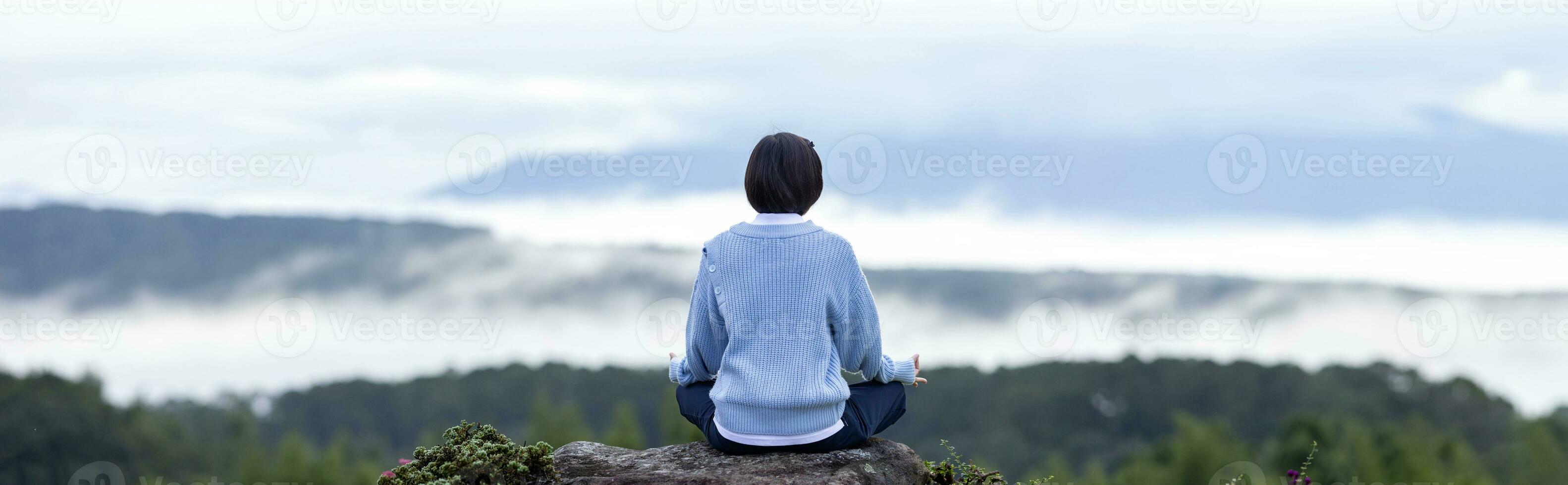 panorama tillbaka se av kvinna i luvtröja är avkopplande praktiserande meditation yoga på de topp av berg med dimma och dimma i sommar till uppnå lycka från inre fred visdom för friska sinne och själ foto