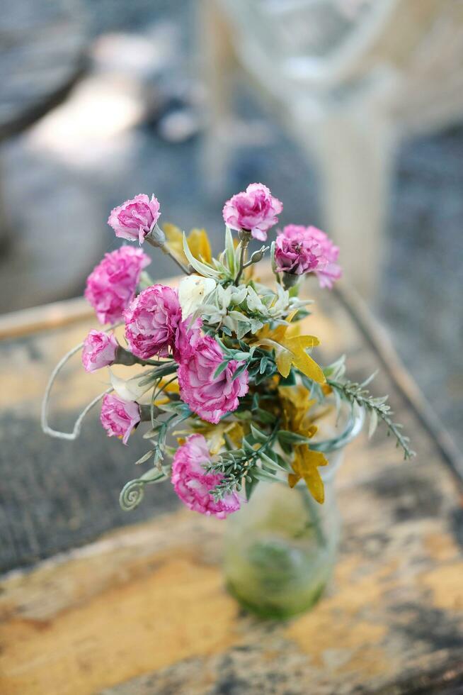 liten blomma rosa blommor i glas vas dekorerad på årgång trä- tabell i naturlig trädgård hus foto