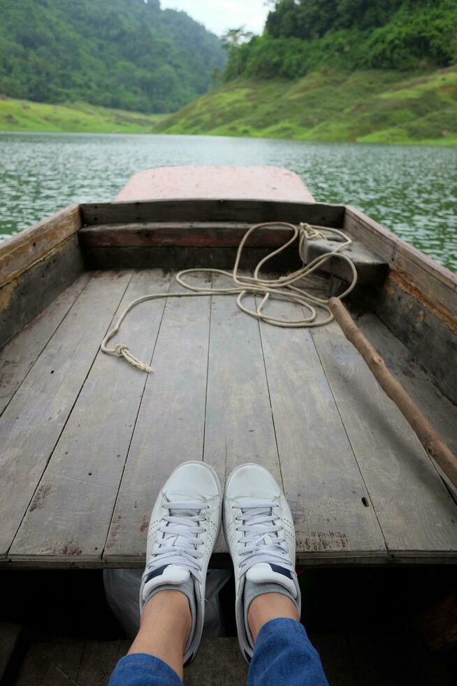 kvinna barfota och gymnastikskor skor är reser och avkopplande på trä- lång svans båt på damm i thailand foto