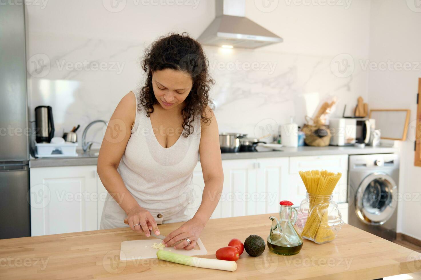 latin amerikan kvinna kock framställning en friska sallad för middag på Hem, hackning vitlök på en skärande styrelse foto