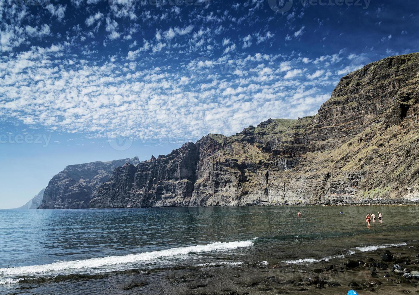 turister som badar vid los gigantes vulkanisk svart sandstrand vid berömda naturliga klippor landmärke i södra tenerife ö spanien foto