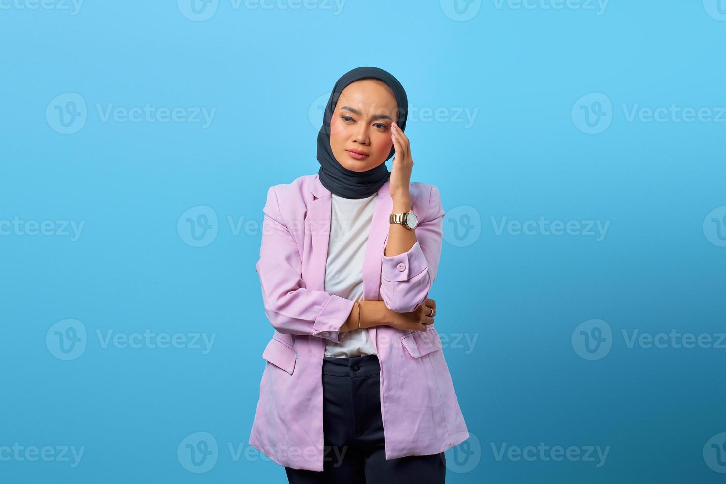 utmattad asiatisk kvinna vidrör hennes smärtsamma öga över blå bakgrund foto