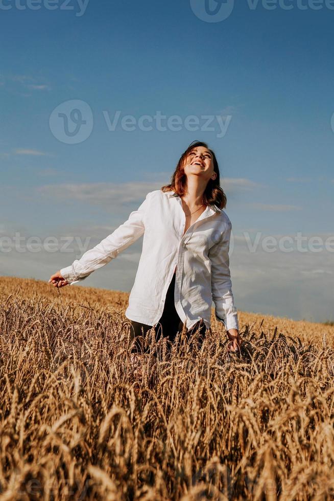 glad ung kvinna i en vit skjorta i ett vetefält. solig dag. foto