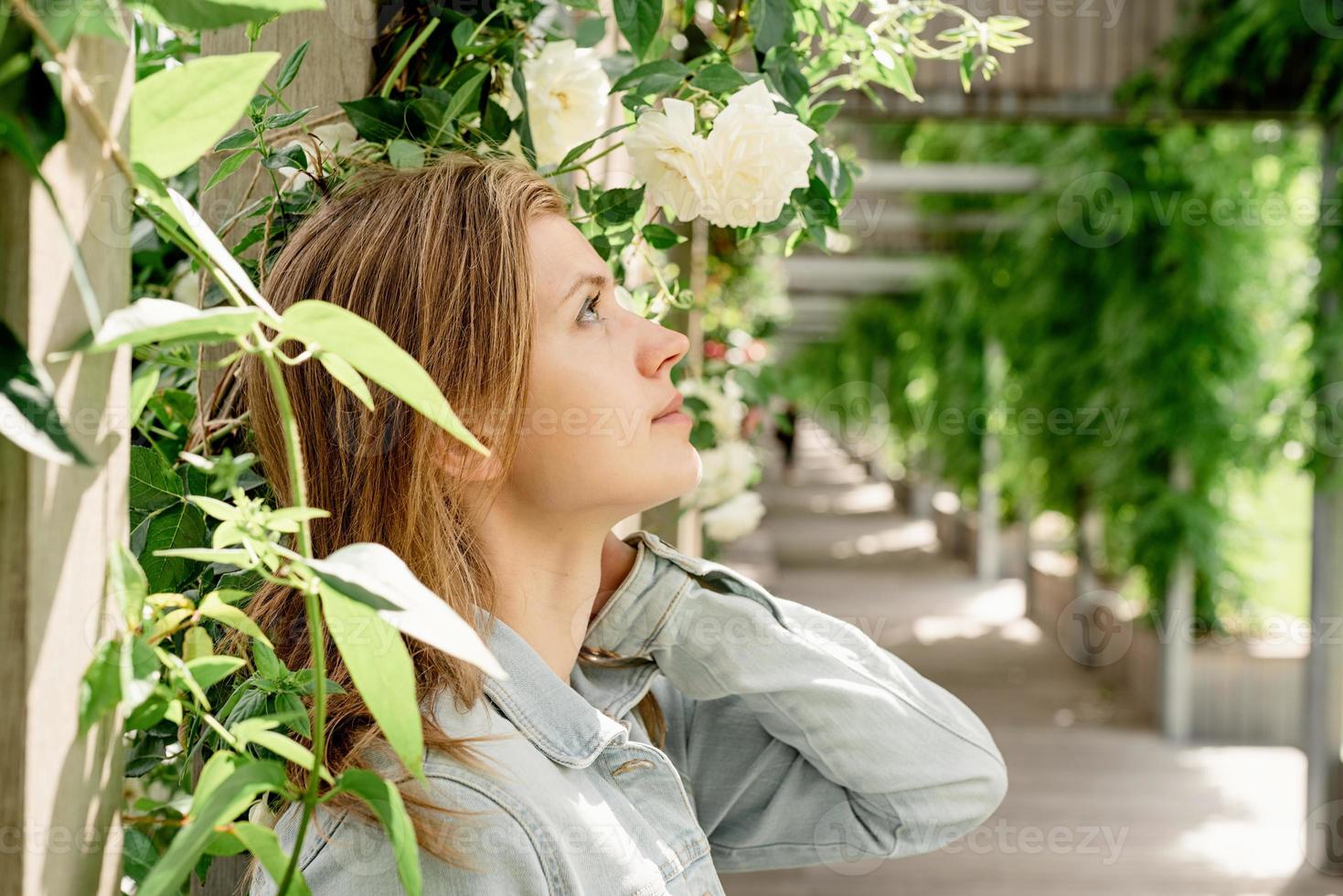 ung kvinna som står i vita rosor i en trädgård eller park foto