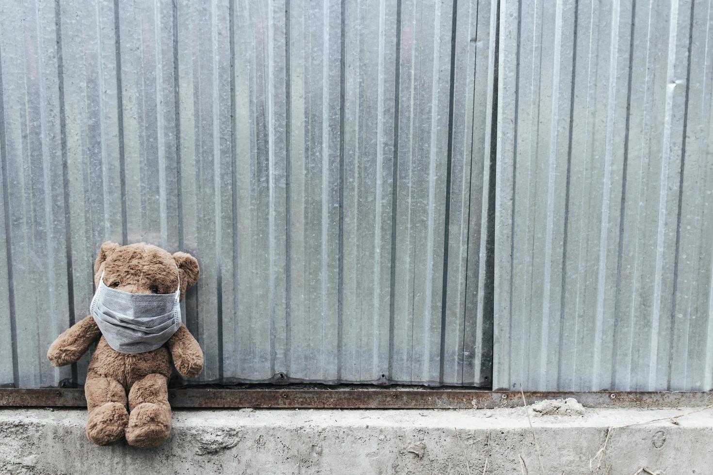 nalle i medicinsk mask sitter nära metallstaket. foto