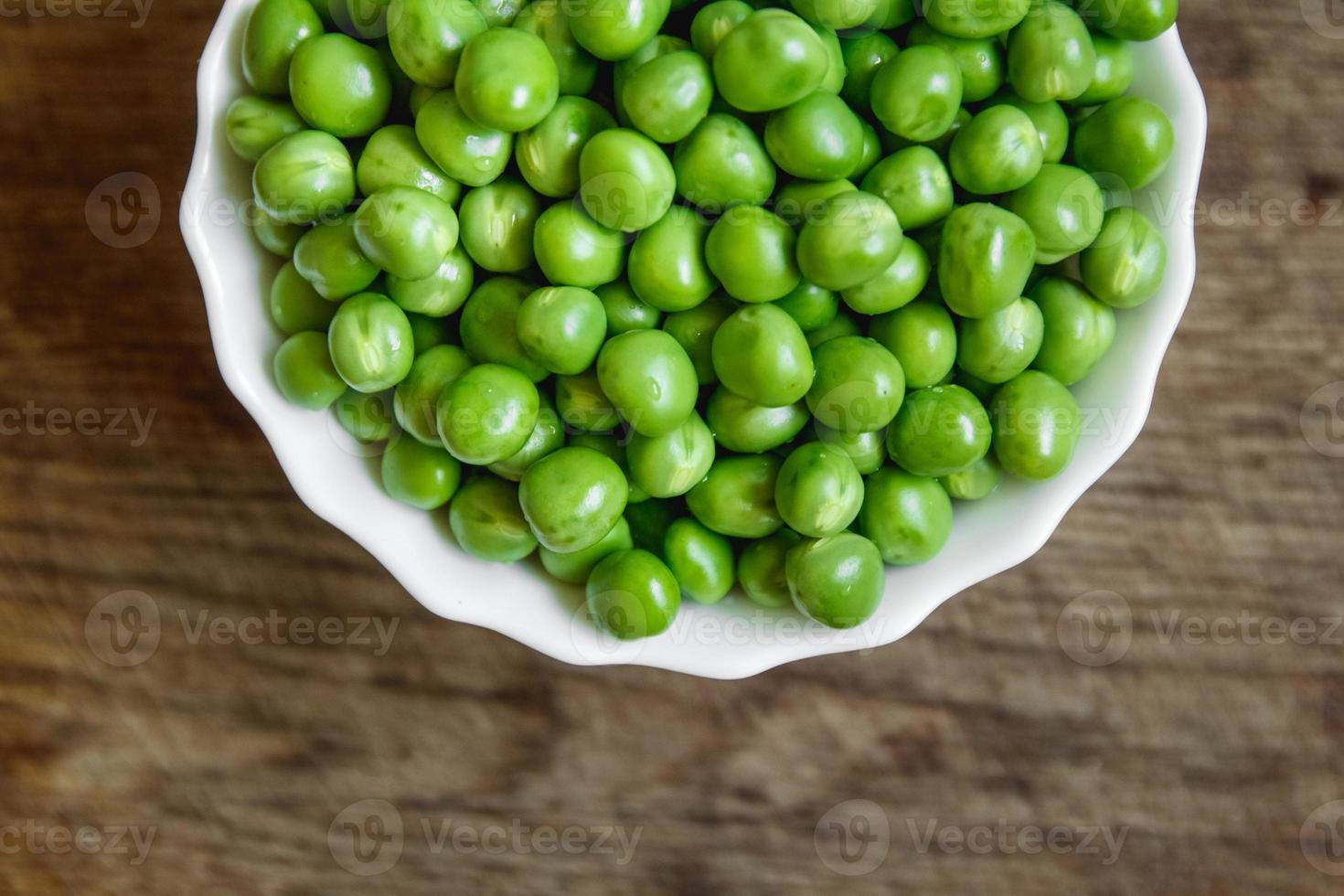 färska gröna ärtor i en vit tallrik på träbakgrund foto