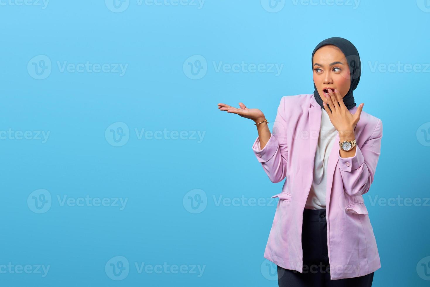 förvånad asiatisk kvinna som visar produkten på blå bakgrund foto