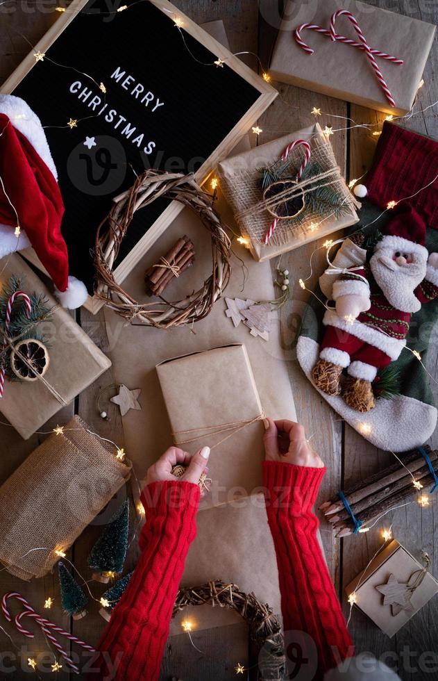 kvinnliga händer som sveper in julklappar i hantverkspapper ovanifrån platt låg foto