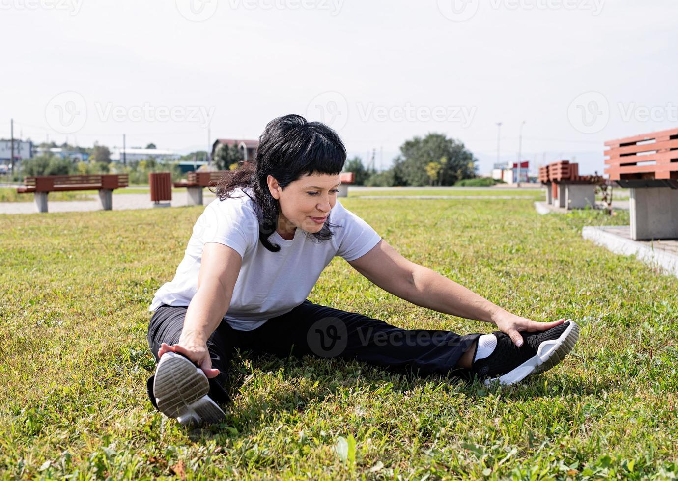 le kvinna värmer upp stretching sitter på gräset i parken foto