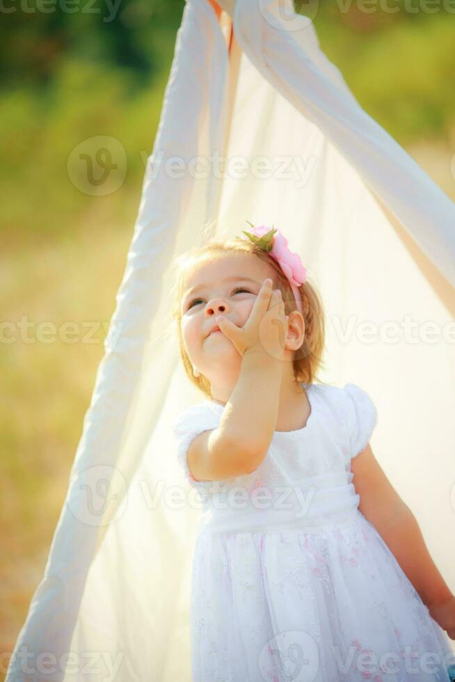 skön flicka i vit festlig klänning innehar på hand och kind se på de himmel. foto