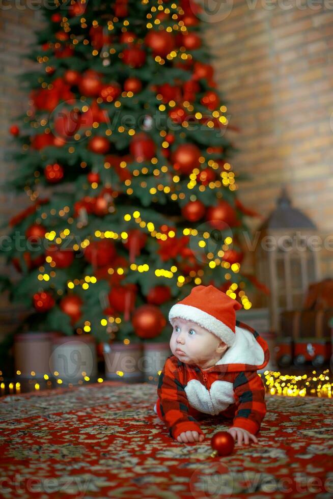 liten överraskad barn i santa kostym i festlig rum på jul eve. flicka på bakgrund av jul träd. foto