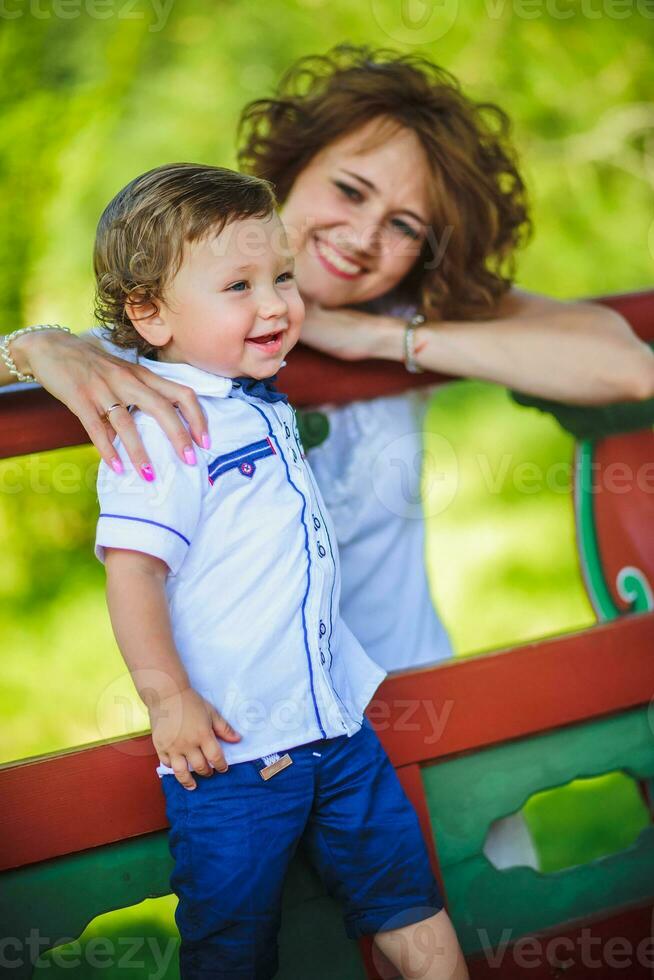 mamma kramar liten son och spelar i parkera på solnedgång tid. människor har roligt på skog. begrepp av vänlig familj och av sommar semester. foto